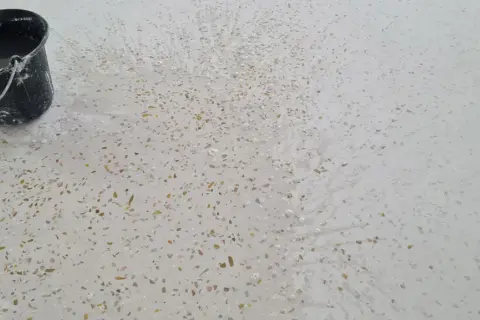 Un seau d'eau éclabousse un sol en terrazzo blanc moucheté, révélant comment faire briller un sol en terrazzo.
