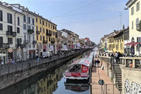 En båt på Navigli i Milano, omgiven av färgglada byggnader och folk som promenerar längs kanalen.