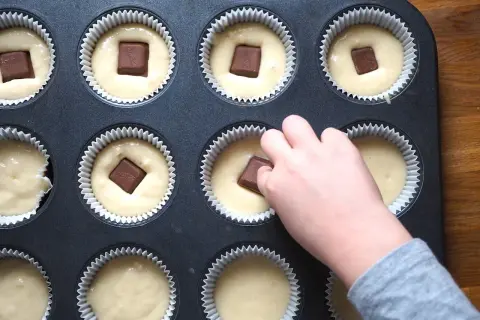 Dziecko wkłada kostkę czekolady do ciasta na muffinki. Prosty sposób, jak udekorować muffinki, by były pyszne.