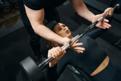 Une femme commence la musculation avec un haltère, guidée par un coach.