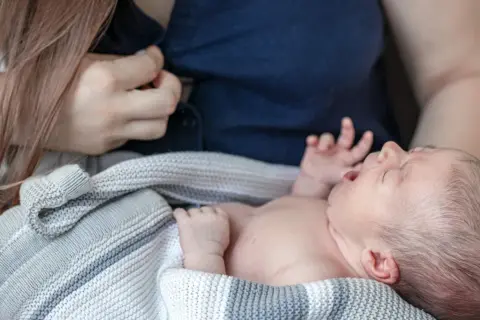 En bebis frustrerad vid amning, med öppen mun och knutna händer, insvept i en stickad filt.
