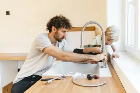 Padre e figlio installano un nuovo rubinetto in cucina, un'operazione che richiede attenzione per spostare attacchi cucina senza rompere pavimento.