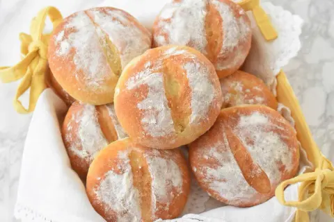Koszyk pełen świeżych, puszystych bułek ziemniaczanych, posypanych mąką. Idealne na śniadanie lub jako dodatek do obiadu.