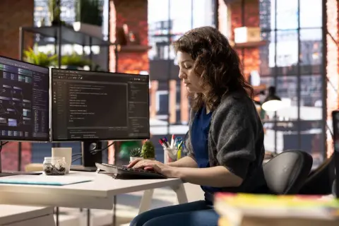Une développeuse code sur deux écrans, explorant a quoi sert Java pour créer des applications complexes.
