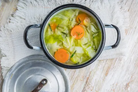 Une marmite de soupe au chou, avec des carottes et des herbes, sur une serviette blanche.