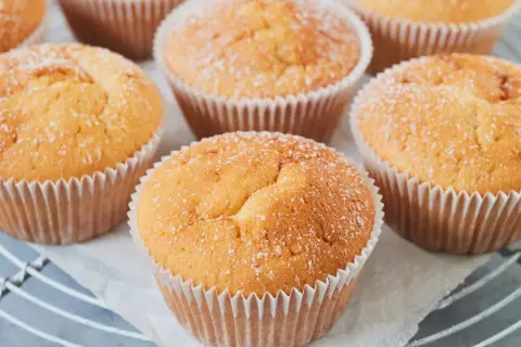 Frisch gebackene Quark Muffins, leicht mit Puderzucker bestäubt, auf einem Gitter.