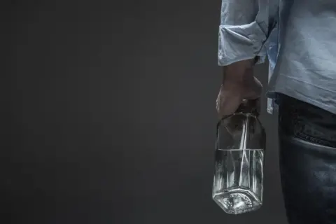 Mężczyzna trzyma butelkę z płynem, sugerującą potencjalną dawkę śmiertelną alkoholu.