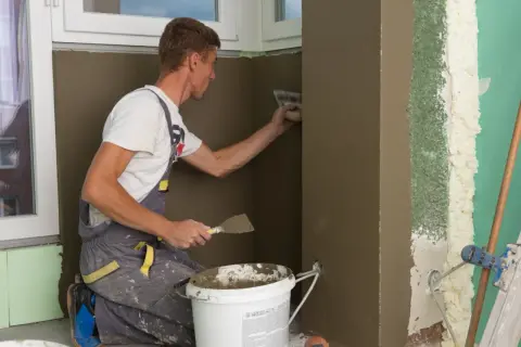 Remont starego domu: fachowiec tynkuje ścianę, pokazując, jak wyrównać ściany w starym domu.