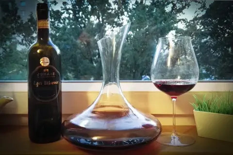 Butelka wina Egri Bikavér, karafka i kieliszek z czerwonym winem. Właściwości tego węgierskiego trunku są cenione przez koneserów.