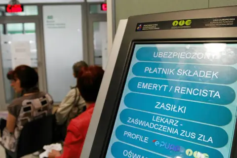 Terminal samoobsługowy w urzędzie, gdzie można uzyskać m.in. zaświadczenie o niezaleganiu ZUS. W tle czekający ludzie.