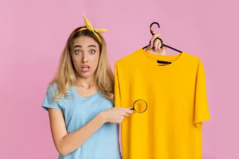 Ragazza sorpresa scopre macchie di detersivo sui vestiti con una lente d'ingrandimento.