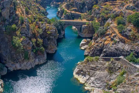 Cañón con río azul y puente de piedra, evocando la belleza natural de los pueblos de Madrid.