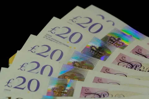 Kilka banknotów 20 funtów aktualnych, ułożonych w wachlarz. Widać holograficzne korony i napisy.