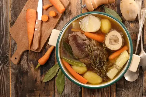 Un bol fumant de pot-au-feu, avec viande, carottes, pommes de terre, oignon et os à moelle. Une recette réconfortante.