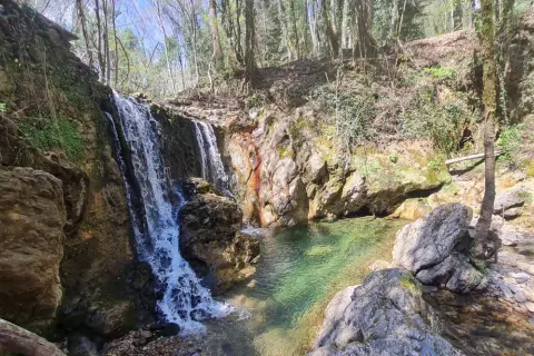 Cascata nella riserva naturale Alto Merse, con rocce colorate e acqua cristallina che forma una pozza verde smeraldo.