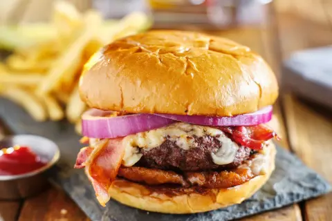 Soczysty burger z bekonem, serem i czerwoną cebulą, podany z frytkami i ketchupem.