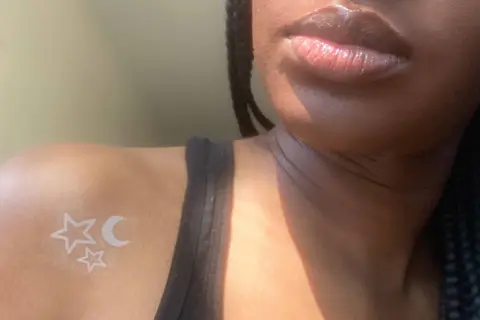 Un delicado tatuaje de tinta blanca con estrellas y luna sobre piel negra, un toque celestial sutil.