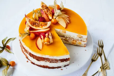 Eine köstliche Maracuja Torte mit frischen Früchten und Sahne. Ein Stück ist bereits angeschnitten, daneben liegen goldene Gabeln.