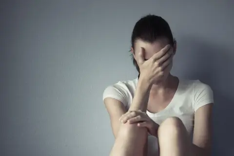 Kobieta siedzi przy ścianie, zakrywając twarz dłońmi. Czasem każdy potrzebuje chwili miansec, by zebrać myśli.