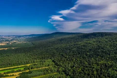 Zielone, leśne góry w okolicach Kielc, z widokiem na pola i błękitne niebo z chmurami.