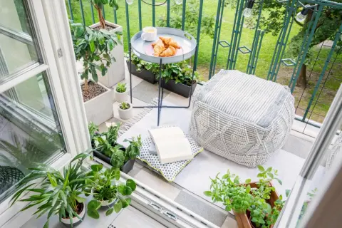 Gemütliche Balkon Ideen: Pflanzen, Kissen, Hocker und ein Tablett mit Croissants laden zum Verweilen ein.