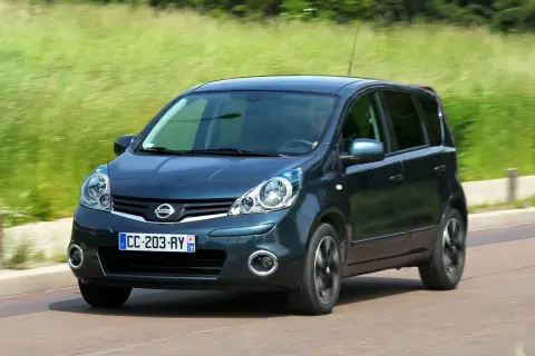 Ciemnozielony Nissan Note E11 w ruchu, z rozmytym tłem zieleni i drogi.