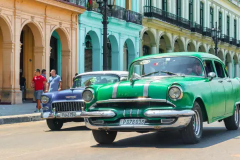Grüne und blaue Oldtimer fahren auf einer Straße in Havanna. Diese Autos sind ein Symbol für die Geschichte und den Charme der Stadt, die man oft bei einem **oldtimer importieren** erleben kann.