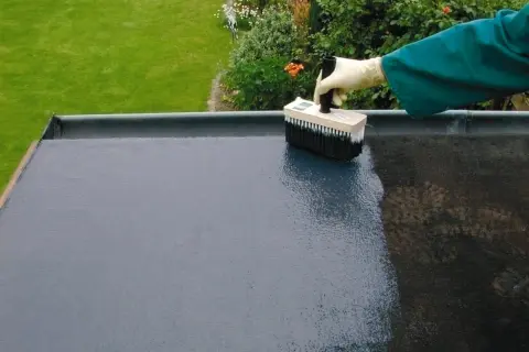 Mit einem Pinsel wird ein Bitumen-Voranstrich auf eine flache Dachfläche aufgetragen.