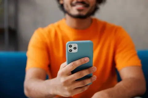 Uśmiechnięty mężczyzna w pomarańczowej koszulce trzyma telefon. Chcesz wiedzieć, jak sprawdzić czas korzystania z telefonu?