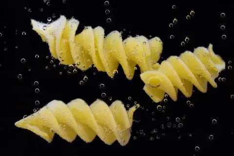 Dwa makarony fusilli gotujące się w wodzie, otoczone bąbelkami. Idealny przykład, jak ugotować makaron.