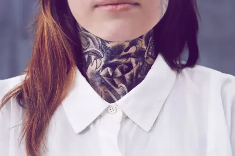 Ein detailreiches, old school Hals Tattoo mit einem Wolfskopf und scharfen Zähnen, bedeckt den Hals einer Person, die ein weißes Hemd trägt.