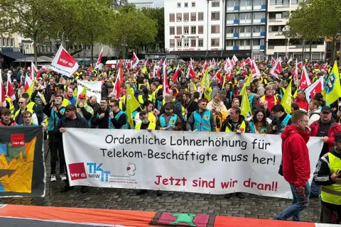 Große Menschenmenge bei einem Telekom-Streik. Sie fordern "Ordentliche Lohnerhöhung für Telekom-Beschäftigte muss her!". Viele Fahnen und gelbe Westen sind zu sehen.