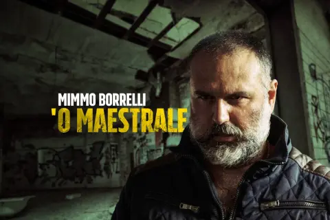 Mimmo Borrelli, 'O Maestrale, in un'ambientazione che ricorda Gomorra, con graffiti e un'atmosfera cupa.