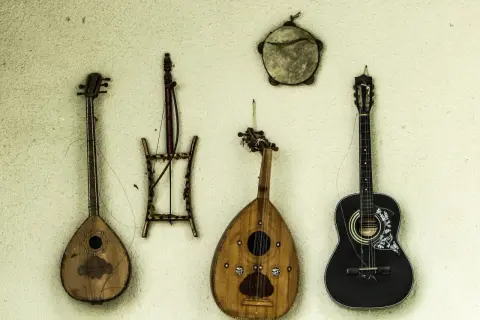 Alte Saiteninstrumente hängen an der Wand. Eine schwarze Gitarre, eine birnenförmige Laute und zwei weitere, wie sie die erste Gitarre aussehen ließen.