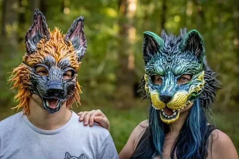 Dwie osoby w maskach wilków, symbolizujące tożsamość therian. Jedna w odcieniach pomarańczu, druga w zieleni i błękicie.