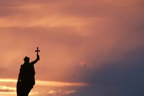 Silueta de estatua con cruz alzada, evocando la gesta de Don Pelayo y la Reconquista, bajo un cielo crepuscular.