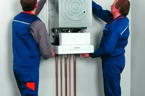 Dwóch techników montuje kocioł gazowy, zapewniając jego zabezpieczenie pieca gazowego przed przepięciem.