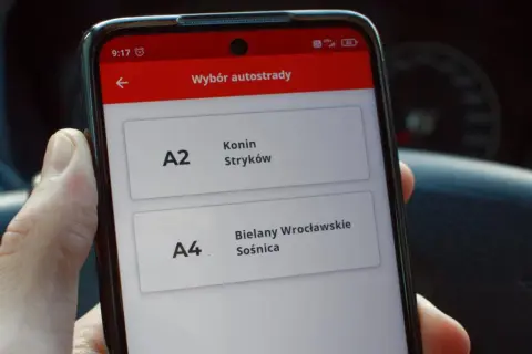 Dłoń trzyma smartfon z aplikacją do wyboru autostrady A2 Konin-Stryków i A4 Bielany Wrocławskie-Sośnica.