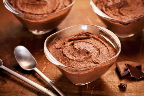 Trois coupelles de mousse au chocolat sans oeuf, onctueuse et gourmande, avec des morceaux de chocolat noir et des cuillères sur fond de bois.