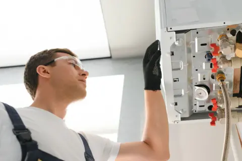Instalator w okularach ochronnych sprawdza podłączenia kotła, gdzie widoczna jest anoda tytanowa.
