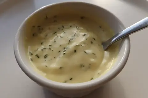 En skål med krämig, gul vegansk bearnaisesås med finhackade örter. Perfekt för ditt veganska bearnaisesås recept.