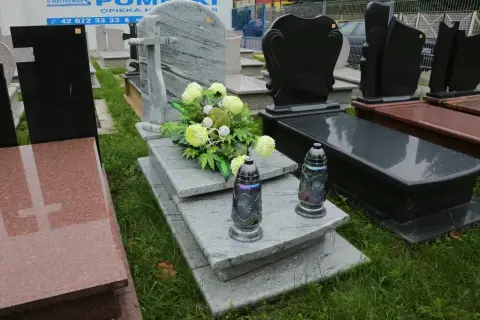 Elegancka dekoracja grobu bez pomnika: szare płyty, bukiet jasnych kwiatów i dwie znicze.