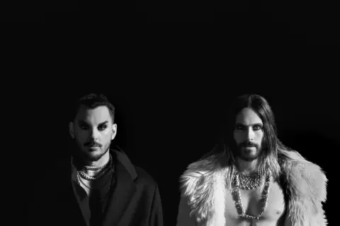 Jared Leto i Shannon Leto z 30 Seconds to Mars na czarno-białym zdjęciu. Jared w futrzanym płaszczu, Shannon w eleganckim płaszczu.