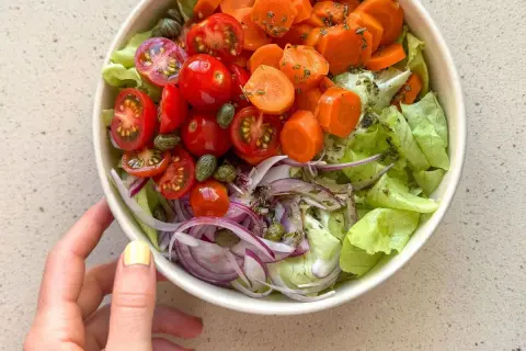 Deliciosa ensalada mediterránea con lechuga, tomates cherry, zanahoria, cebolla morada y alcaparras.