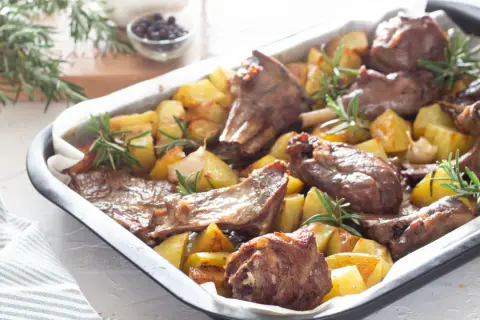 Agnello al forno marinato con patate e rosmarino, un piatto succulento e profumato, pronto per essere gustato.