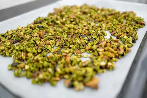 Granola claire au matcha, parsemée d'amandes et de graines, prête à être cuite sur une plaque de cuisson.