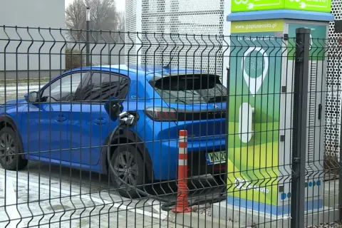 Niebieski samochód elektryczny podłączony do ładowarki. Zastanawiasz się, ile waży samochód elektryczny? Ten model jest lekki i ekologiczny.