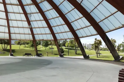 Estructura de madera y cristal en el parque de Eiris, con vistas a césped, árboles y edificios.