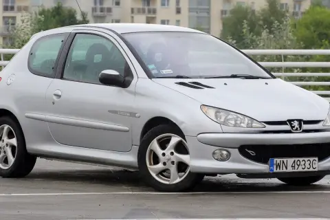 Srebrny Peugeot 206 na mokrym parkingu, z widocznym numerem rejestracyjnym WN 4933C.