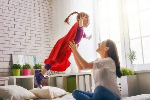 Mama rzuca córkę w stroju superbohaterki w powietrze. Radość i zabawa w pokoju.